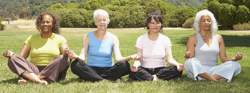 Two people meditating in a park on a sunny day.