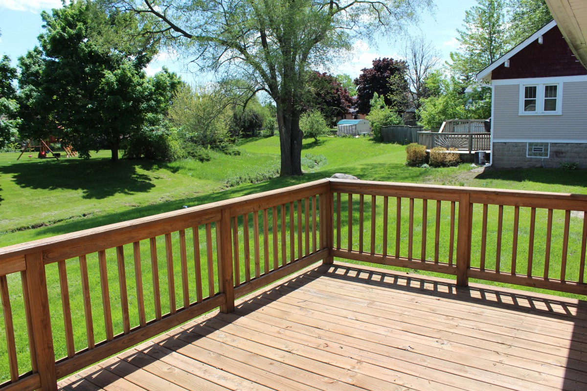 A sunny backyard view from a wooden deck, featuring lush green grass and trees.