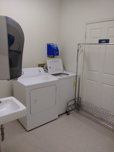 A clean and organized laundry room featuring a washing machine, dryer, sink, and clothes rack.