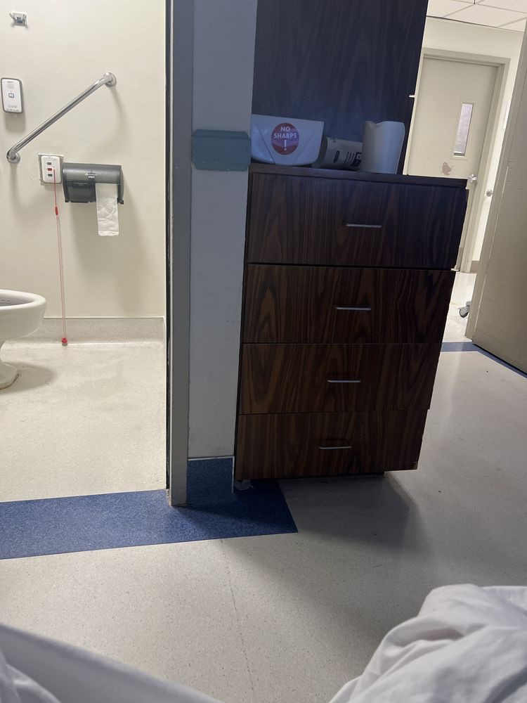 A view of a hospital room bathroom, featuring a cabinet and safety handrails.