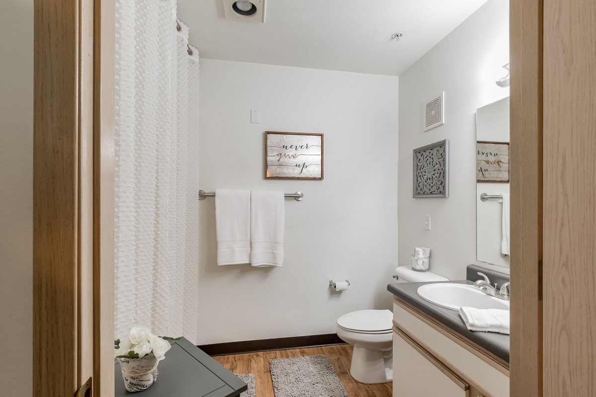 A clean and simple bathroom with white walls, featuring a sink, mirror, toilet, and neatly hung towels.