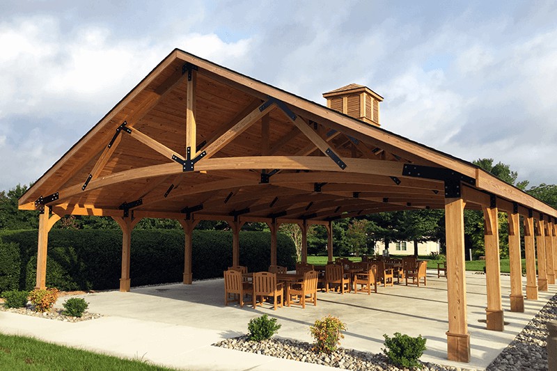 A wooden pavilion with outdoor seating under a clear sky.