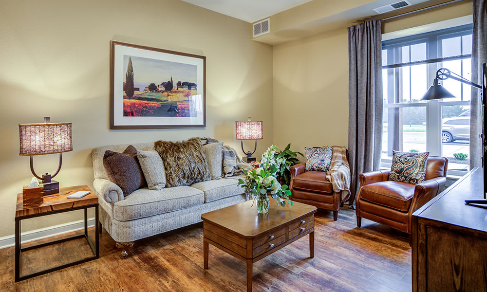 A cozy living room with a sofa, armchairs, and a coffee table, accented by a large painting and natural light filtering through the curtains.