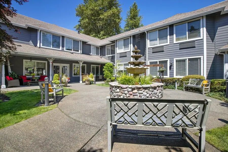 A sunny courtyard with a central fountain surrounded by a two-story building and outdoor seating.