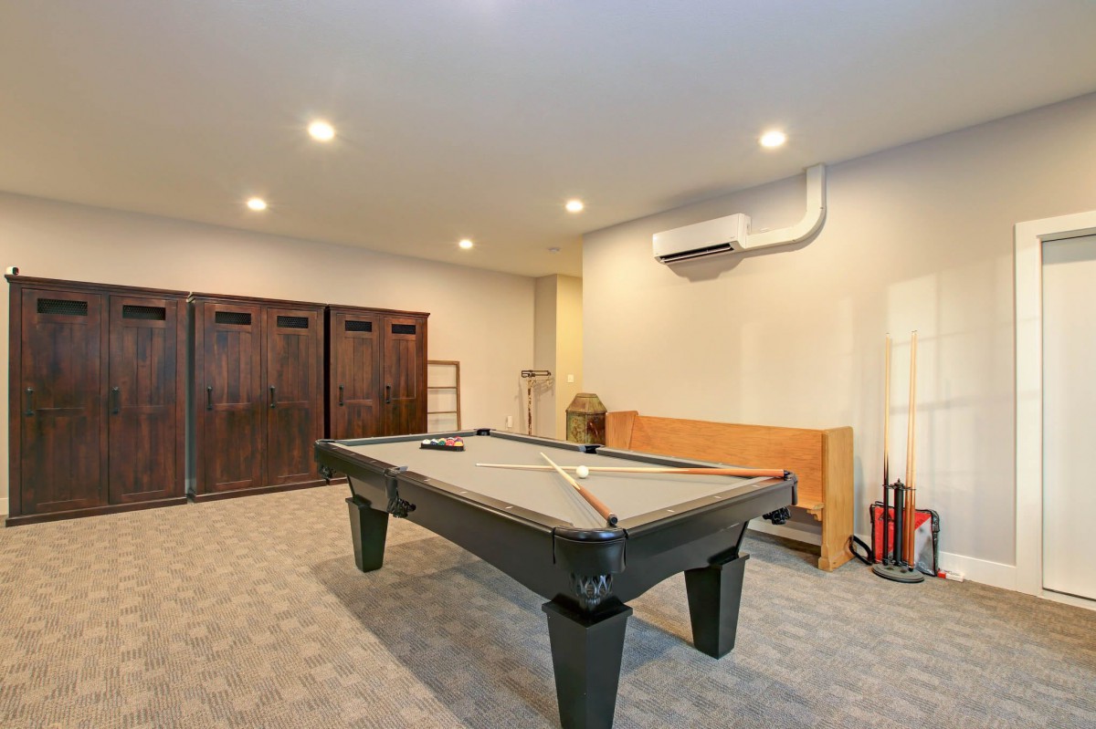 A spacious game room featuring a pool table, wooden lockers, and carpeted flooring.