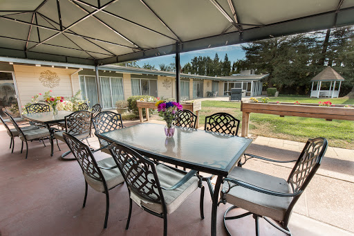 A cozy outdoor dining area with a table and chairs under a canopy, surrounded by greenery.