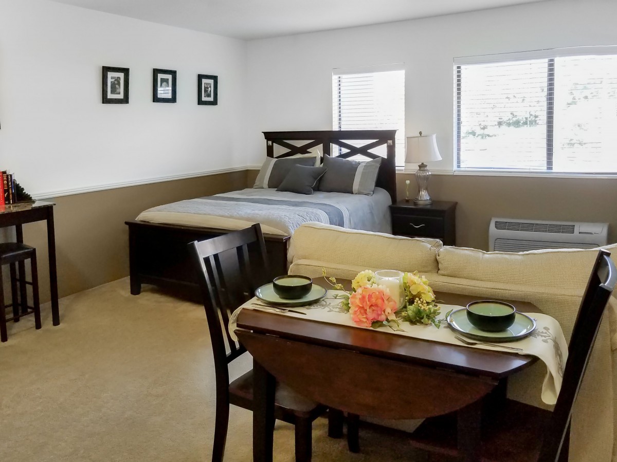 A minimalist bedroom with a cozy bed and a small dining area.