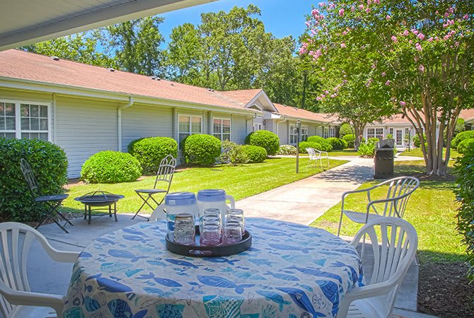 A sunny outdoor patio with a table and chairs, overlooking a well-maintained garden.