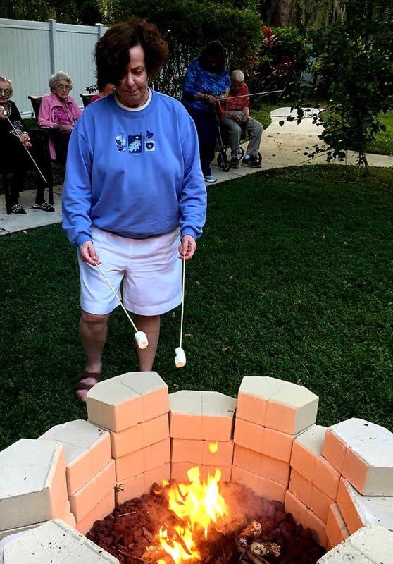 A person is roasting marshmallows over a fire pit in an outdoor gathering.