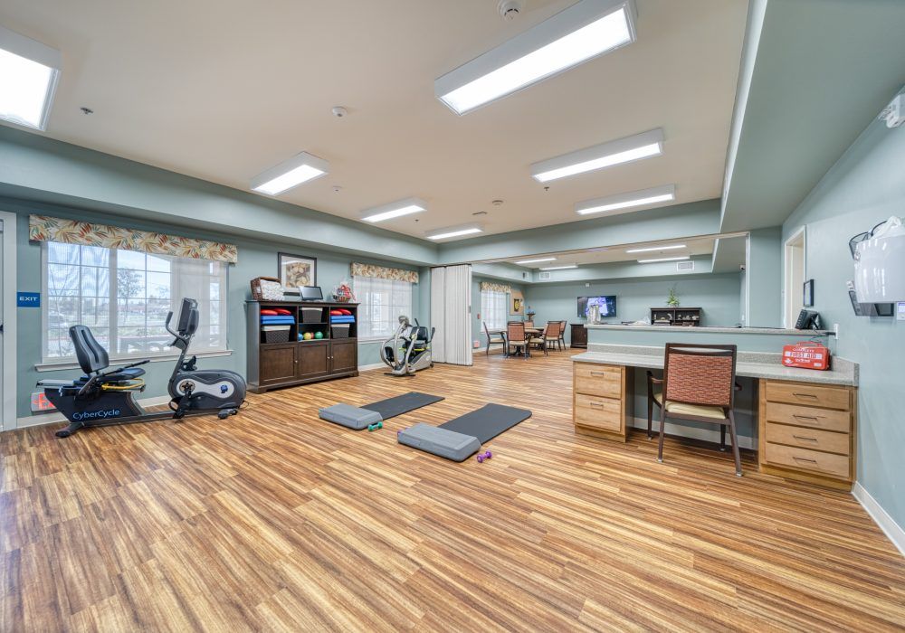 A well-equipped gym with exercise equipment and yoga mats on a wooden floor.