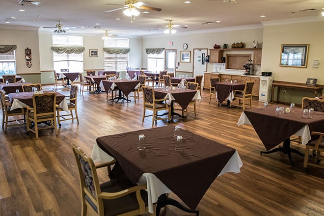 An empty dining room with neatly arranged tables and chairs, featuring a wooden floor.