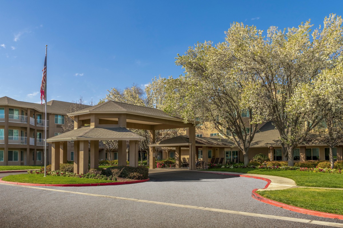 A sunny view of a building entrance surrounded by trees and landscaped grounds.