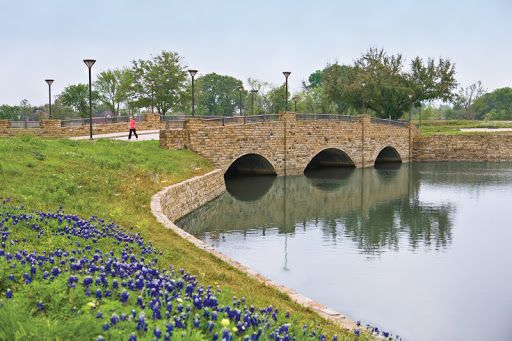 A serene view of a stone bridge arching over calm waters, surrounded by colorful flowers and greenery.