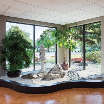 A serene indoor zen garden features a rock arrangement and lush plants, illuminated by natural light streaming through large windows.