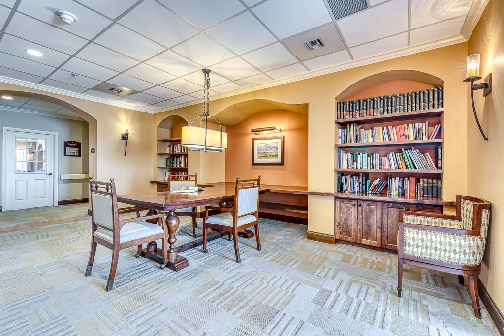 A cozy library room with bookshelves, a wooden table, and chairs under warm lighting.