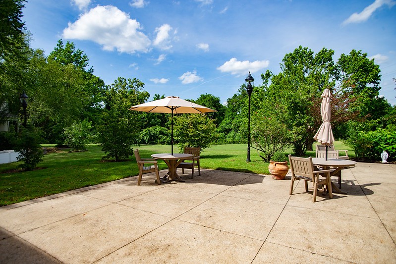 A sunny patio with outdoor furniture and an umbrella overlooking a lush garden.