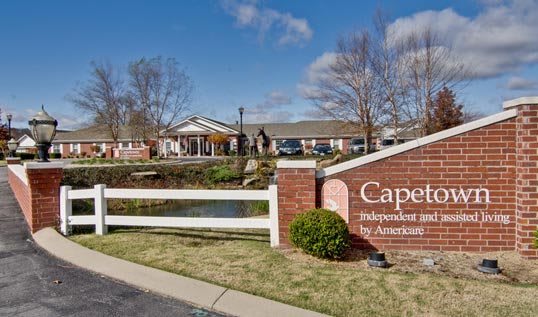 A scenic view of a retirement home with a sign in the foreground and greenery surrounding the area.