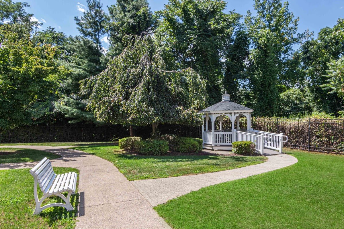 A serene garden with a white gazebo, surrounded by lush greenery and trees.