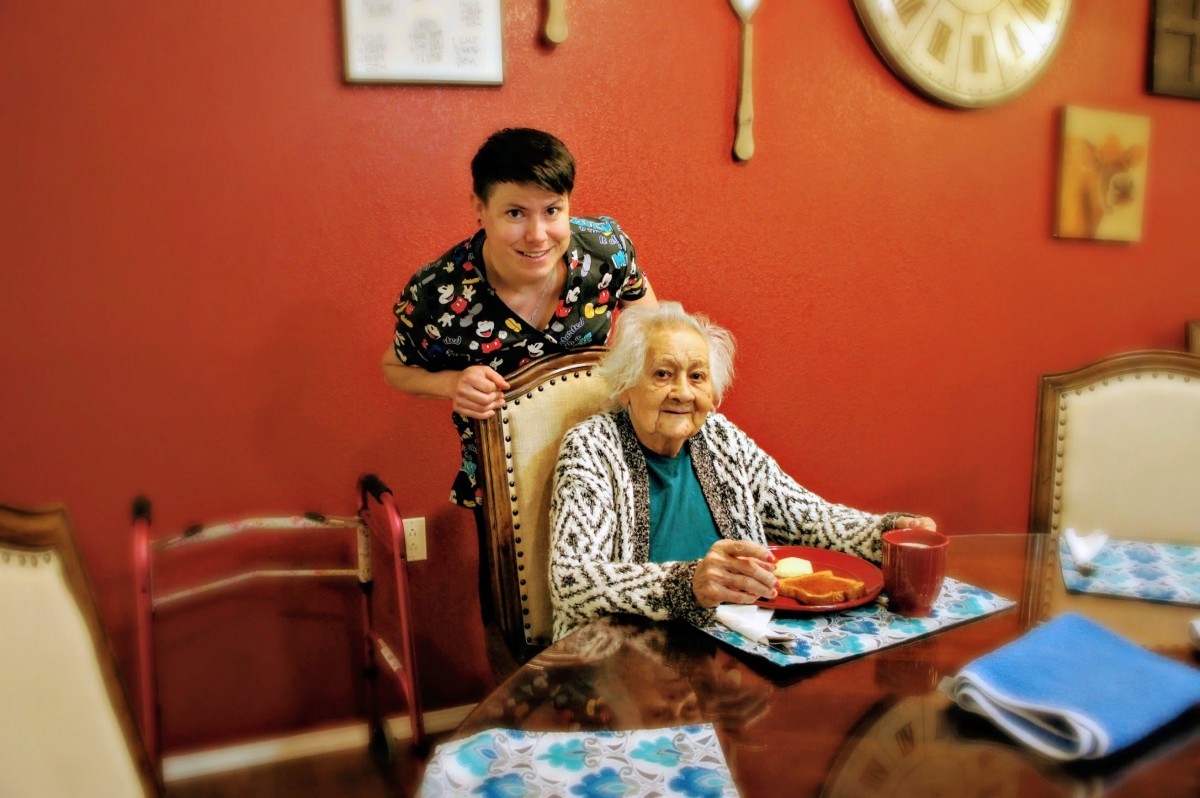 A family member posing with an elderly woman at the dining table.