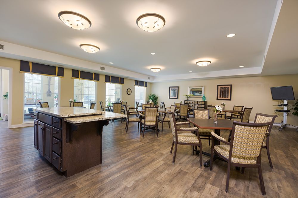 A spacious dining area with multiple tables and chairs, featuring wooden floors and ceiling lights.