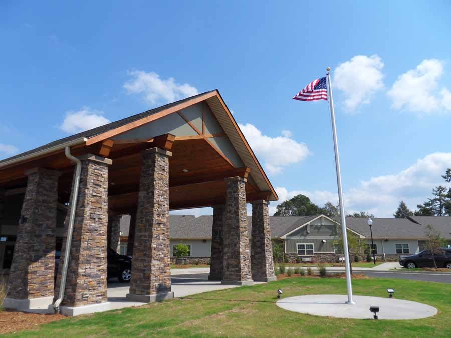 A structure with stone columns and a peaked roof, featuring an American flag on a pole nearby under a clear blue sky.