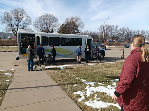 A group of people waiting at a bus stop on a chilly day, with some snow still visible.