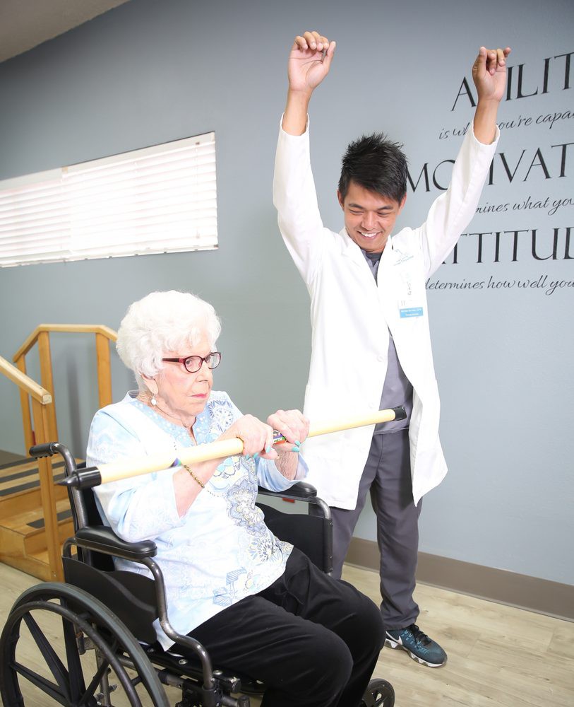 A healthcare professional assists an elderly woman in physical therapy exercises.