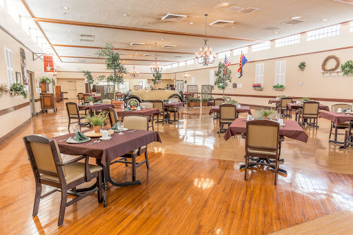 A spacious dining area featuring elegantly arranged tables and chairs, complemented by decorative plants and warm wooden flooring.