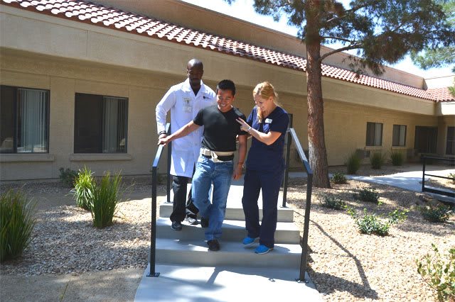 Medical professionals assist a patient with walking exercises outdoors.