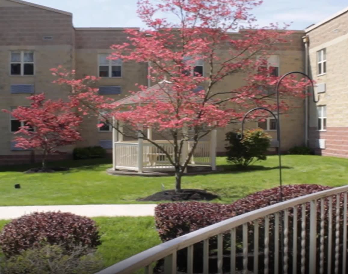 A quaint gazebo surrounded by red-leaved trees and lush greenery in front of a building.
