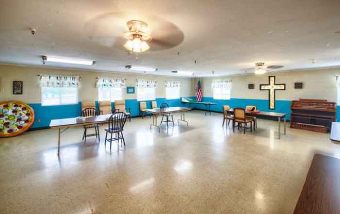 A spacious room with chairs, tables, and a cross on the wall.