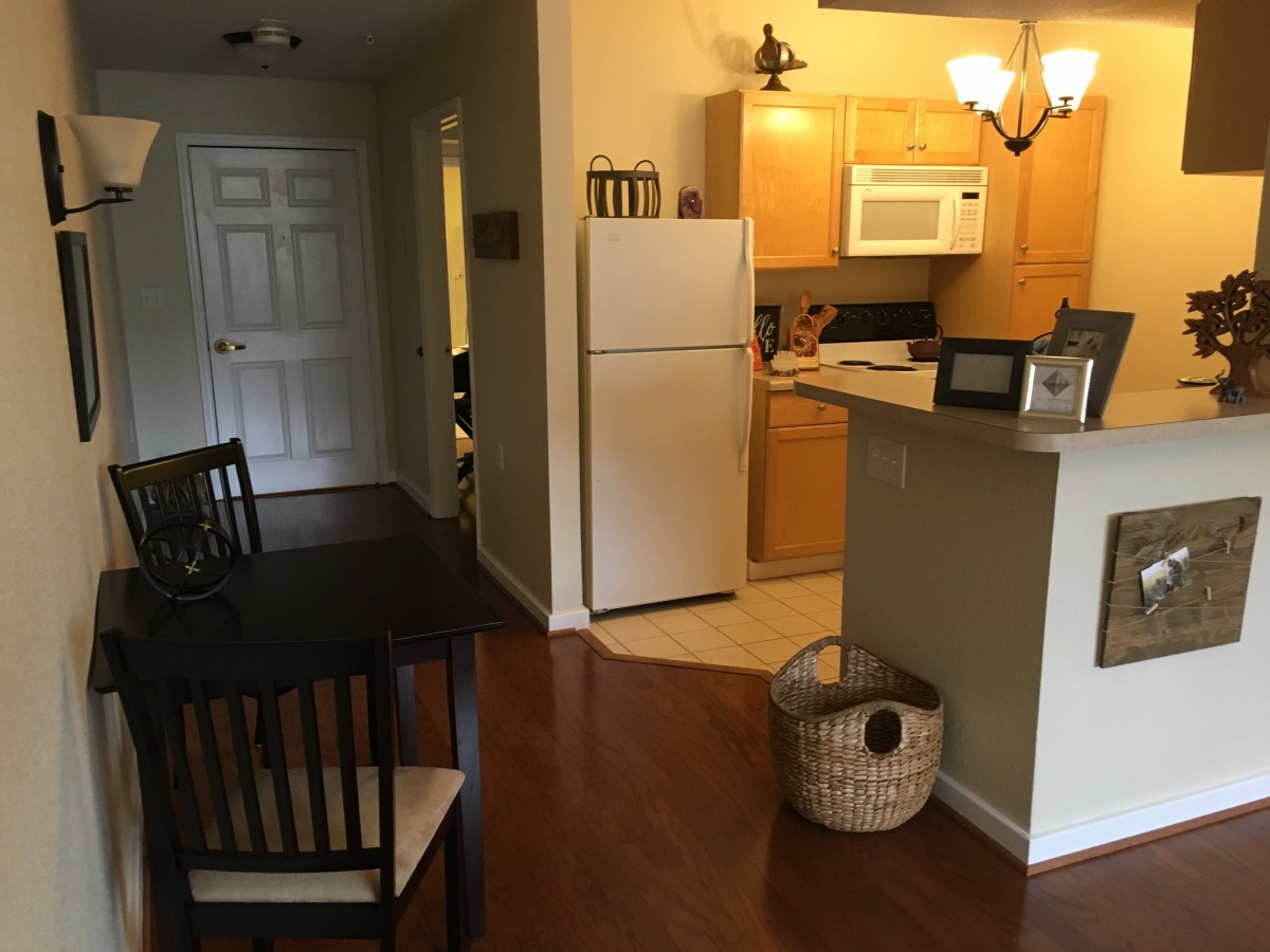 A cozy apartment kitchen with wooden flooring, featuring a dining table, refrigerator, and microwave.