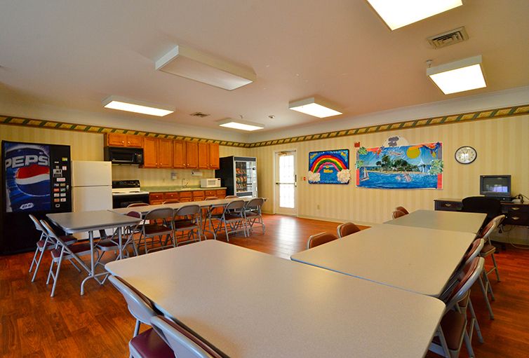 A community meeting room with tables, chairs, and a small kitchen area.