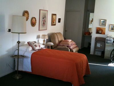 A cozy bedroom with a bed covered in an orange blanket, a sofa, and artwork on the walls.