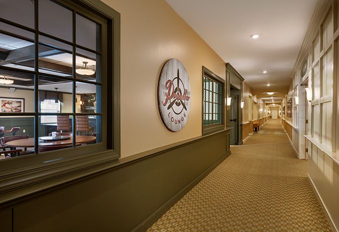 A well-lit hallway with carpeted flooring and windows, featuring a sign on the wall.