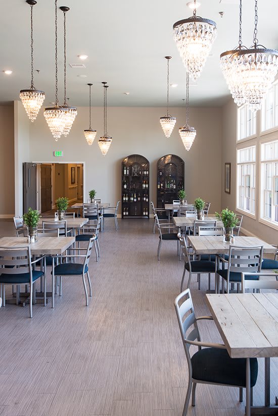 A modern dining area with sleek tables and chairs, illuminated by elegant chandeliers and natural light.