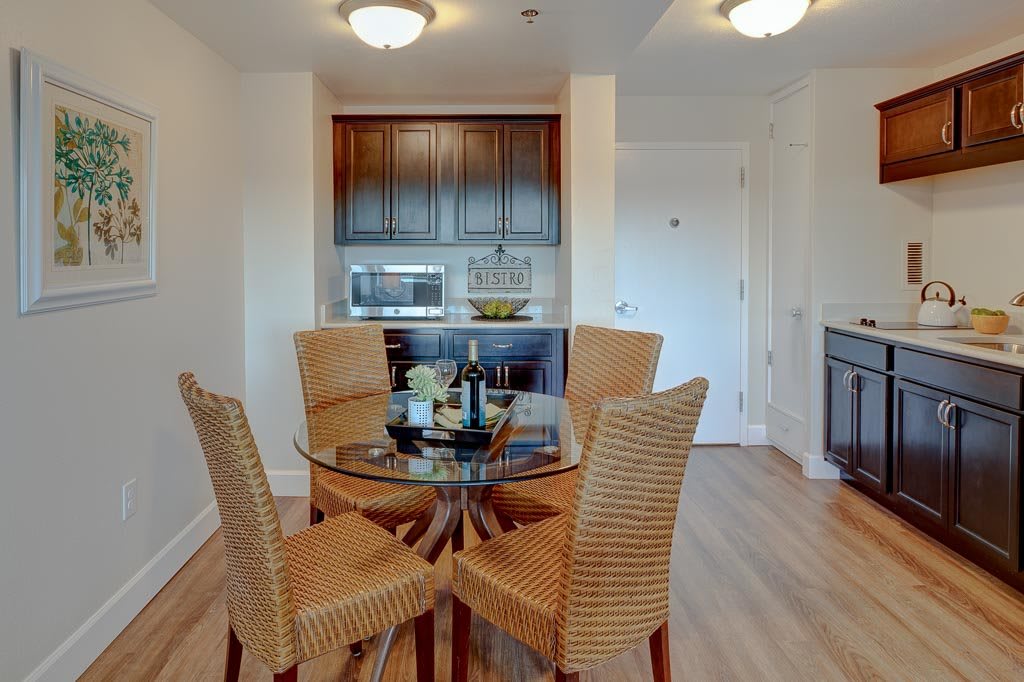 A cozy dining area featuring a glass table with wicker chairs, adjacent to a kitchenette with wooden cabinets.