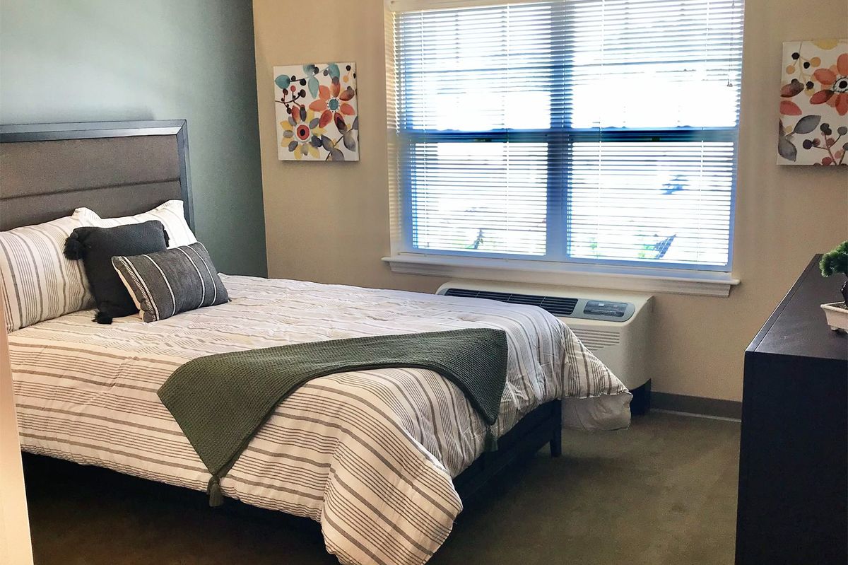 A cozy bedroom with a neatly made bed, decorative pillows, and light streaming through a window.