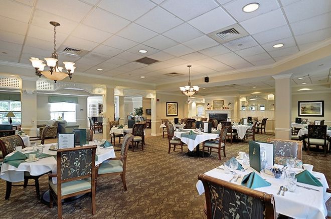 An elegant restaurant dining area with neatly arranged tables and chairs, featuring chandeliers and a carpeted floor.