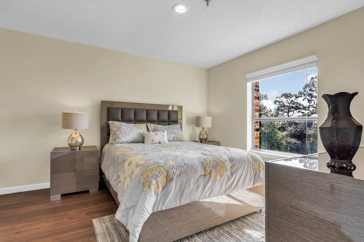 A cozy bedroom with a large bed, lamps on bedside tables, and natural light streaming through a window.
