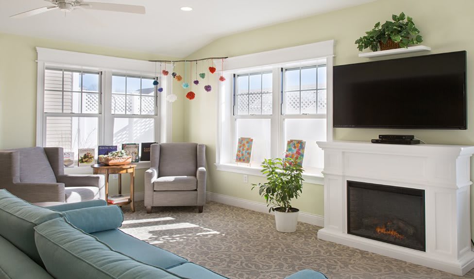 A cozy living room with modern furniture, bright sunlight streaming in through large windows, and a neatly arranged decor.