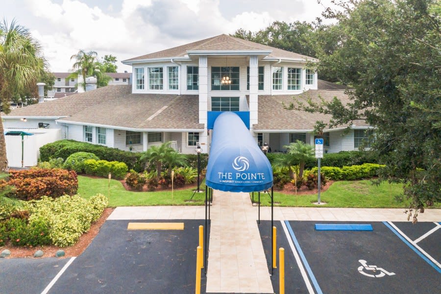 A well-maintained building with a blue awning at the entrance, surrounded by landscaped greenery.