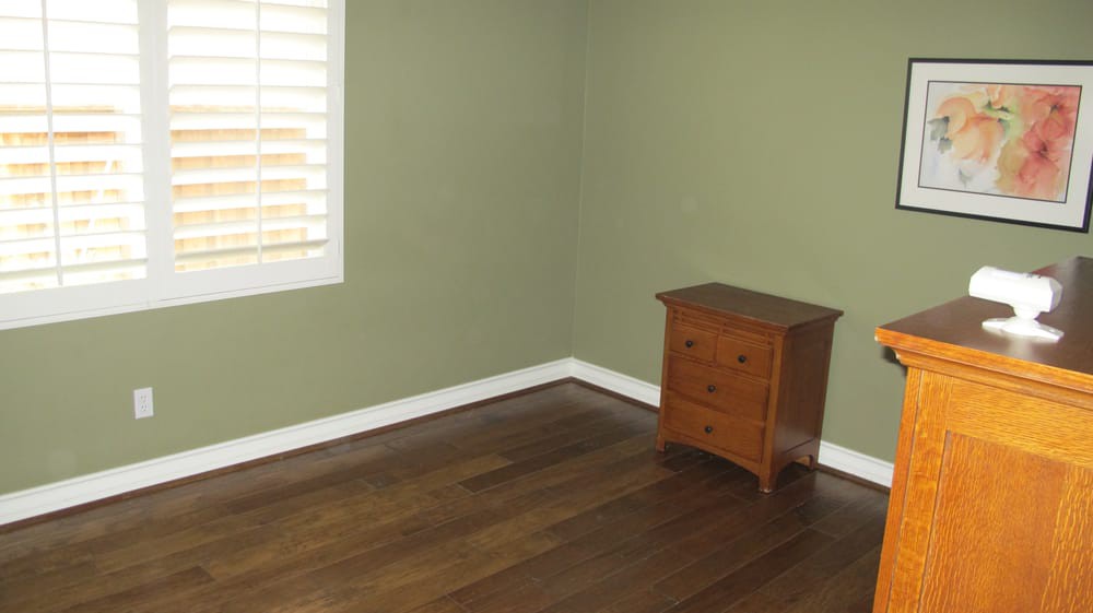 A minimalist room with green walls, a wooden floor, and a small dresser by the window.