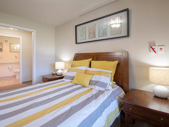 A cozy bedroom with striped bedding, wooden furniture, and a decorative wall frame.