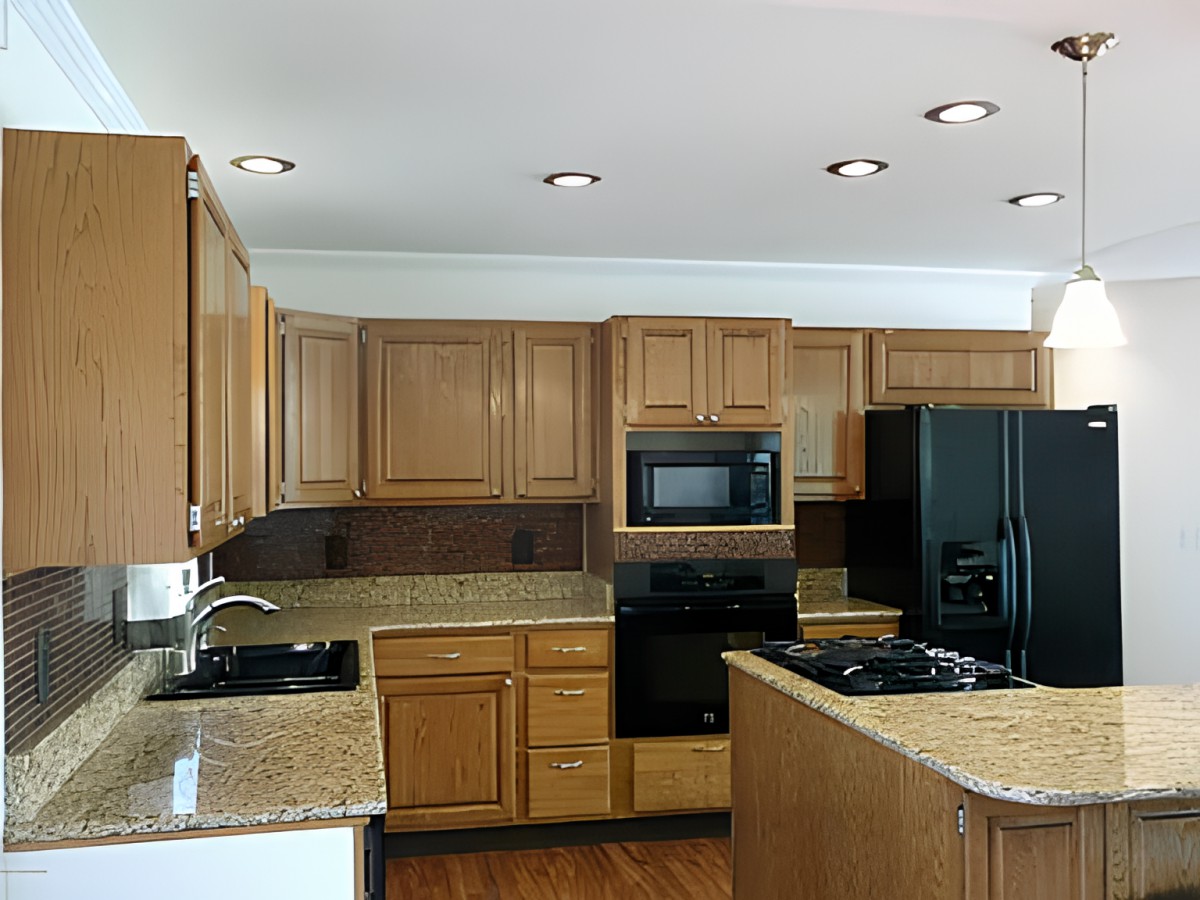 A modern kitchen featuring wooden cabinets, granite countertops, and black appliances including a microwave, oven, refrigerator, and stove.