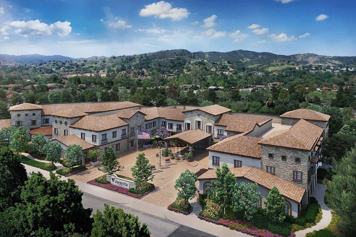 Aerial view of a residential building complex surrounded by lush greenery and hills.