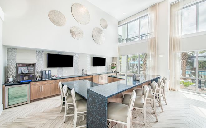 A modern kitchen with a large island and bar stools, featuring TV screens and decorative wall art.