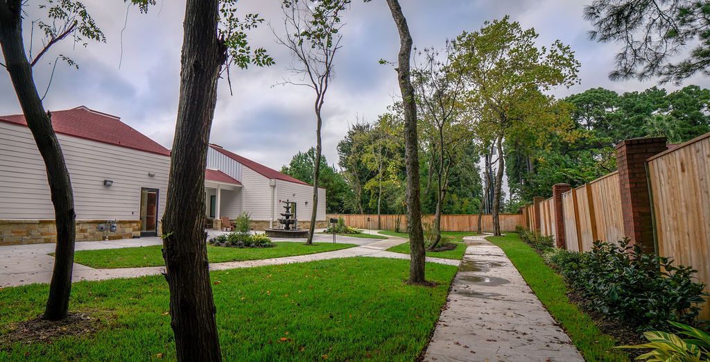 A serene backyard with a well-maintained garden, featuring a house, trees, and a concrete pathway surrounded by lush grass.