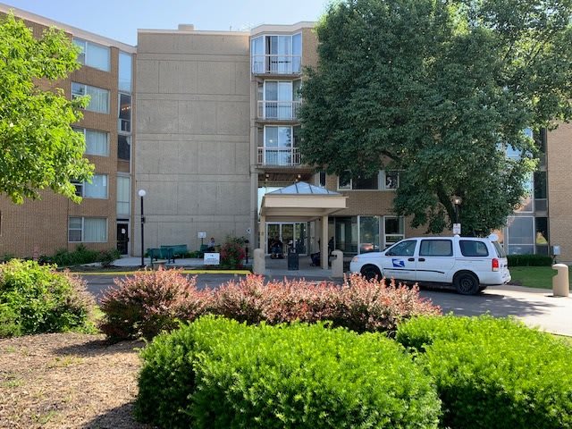 The entrance of a hotel with a car parked nearby and surrounding greenery.