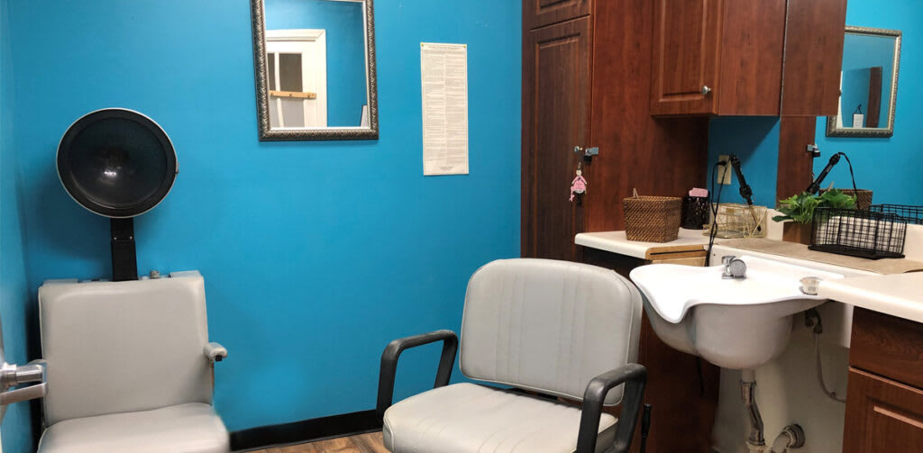 A small waiting area with a chair, mirror, and cabinet against a blue wall.
